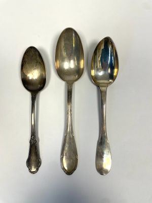 three silver spoons are lined up on a white surface