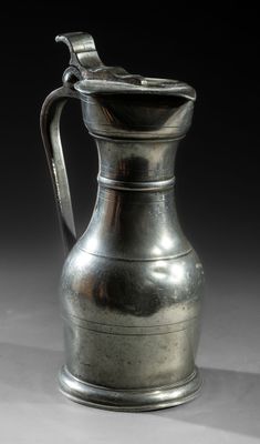 an old silver pitcher sitting on top of a white table