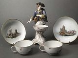 a figurine of a man on a pedestal next to three cups and saucers