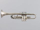 an old silver trumpet hanging from a string on a gray background