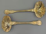 two gold spoons with ornate designs on them sitting on a gray surface