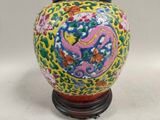 yellow and red vase with a dragon on it on a wooden stand