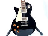 a black electric guitar sitting on a stand on a white surface