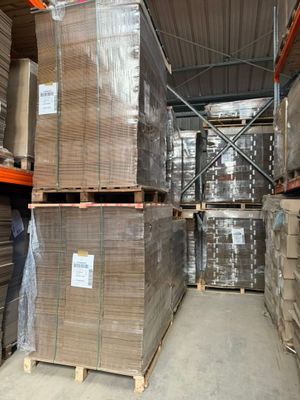 des cartons empilés sur des palettes dans un entrepôt, avec un homme debout à côté d'eux