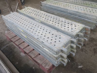 Plusieurs pièces métalliques sont empilées sur des palettes dans un entrepôt