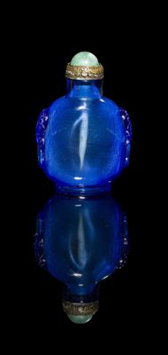 blue glass snuff bottle sitting on a reflective surface with a black background