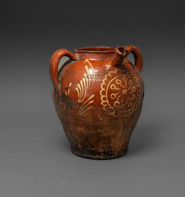 an old brown vase with designs on it sitting on a gray surface