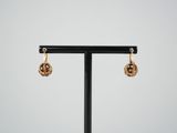 a pair of gold earrings on a black stand