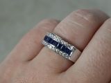 a woman ' s hand holding a diamond and blue sapphire ring