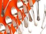 de nombreuses cuillères et fourchettes en argent sur un fond orange et blanc