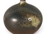 un vase marron et noir posé sur une surface blanche