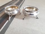 two silver dishes sitting on a striped table cloth