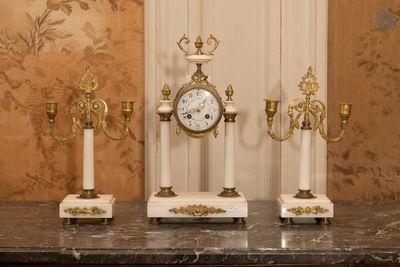 trois bougies et une horloge posées sur une table devant un mur