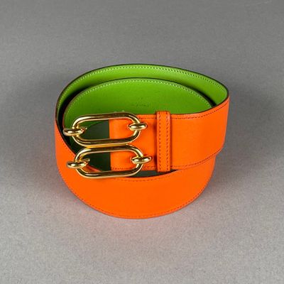 une ceinture orange et verte ornée de deux boucles dorées sur un fond gris