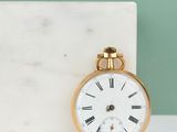 gold pocket watch with roman numerals sitting on a marble block