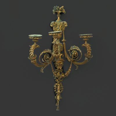 an image of a gold plated three light wall sconce on a black background