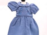 une robe bleue pour une poupée posée sur un socle noir, sur fond blanc