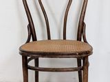 an image of a wooden chair with wicker seat against a white wall