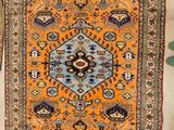 un tapis oriental orange et bleu posé sur un sol blanc, à côté d'une plante verte