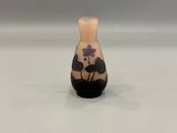 a small vase sitting on a white surface with a purple flower on it