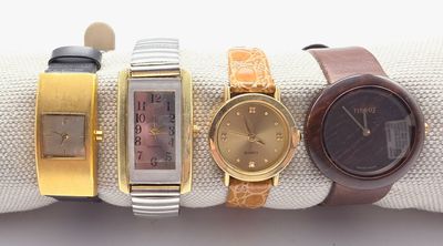quatre montres différentes posées sur un tissu blanc, ornées de bracelets dorés et argentés