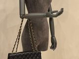 mannequin holding a black chanel bag and a black purse