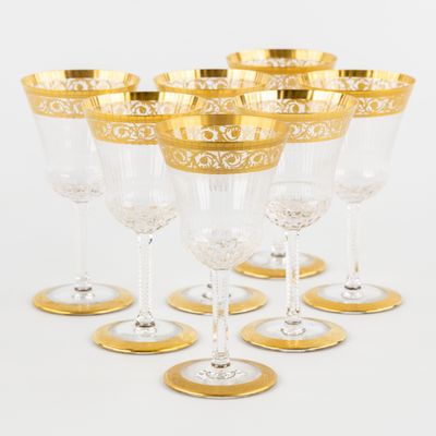 six verres à vin à bordure dorée sont alignés sur une surface blanche