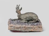 statue of a goat laying on a rock on a white background