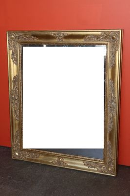 une image représentant un miroir à cadre doré posé contre un mur rouge