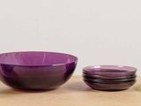 purple and green glass bowls and cups sitting on a wooden table