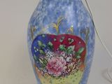 un vase bleu orné de fleurs, sur lequel est posée une lampe allumée