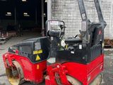 an image of a red and black road roller parked in front of a building
