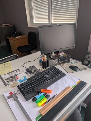 a desk with a computer, keyboard, phone, and other office supplies on it