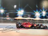 photo dédicacée d'une voiture de course rouge sur un circuit, avec des lumières en arrière-plan