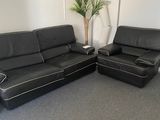 deux canapés en cuir noir et un fauteuil dans une pièce où se trouve une plante