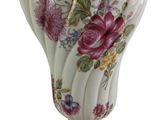 a white vase with pink flowers on it on a gold stand