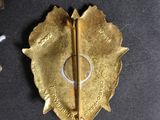 a gold brooch on a black cloth with a gold pin
