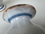 a white and blue vase sitting on a table next to a cup