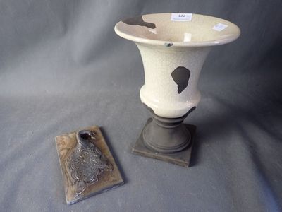 a white vase with a black design on it next to a plaque