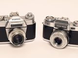 two old cameras sitting side by side on a white surface