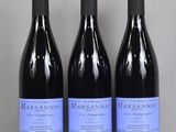 three bottles of wine sit on a glass table in front of a gray wall
