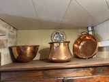 several copper pots and pans sit on top of a wooden cabinet