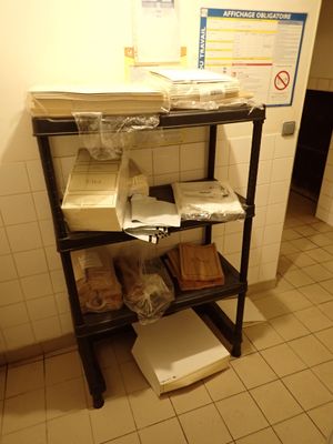 une étagère noire sur laquelle sont posées des boîtes et des sacs, dans une salle de bains