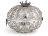 une boîte en argent finement décorée, surmontée d'un oiseau, sur fond blanc