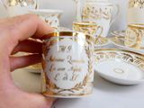 une personne tenant une tasse et une soucoupe devant un ensemble de tasses et de soucoupes