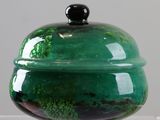 a green glass container with a black lid on a table