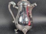 a silver coffee pot with a red handle on a table