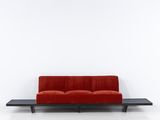 a red couch sitting on top of a black table next to a white wall