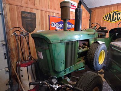 a green tractor parked in a garage with other vehicles