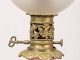 a pink vase with a gold base and a glass lamp on it